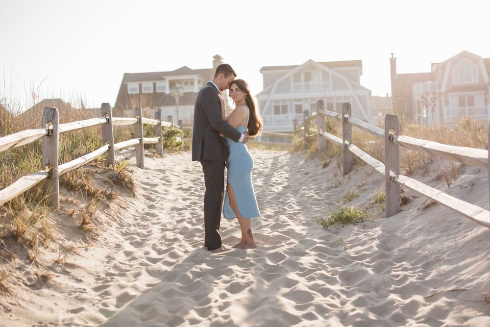 Romantic beach path portrait with couple embracing at sunset near wooden fence.