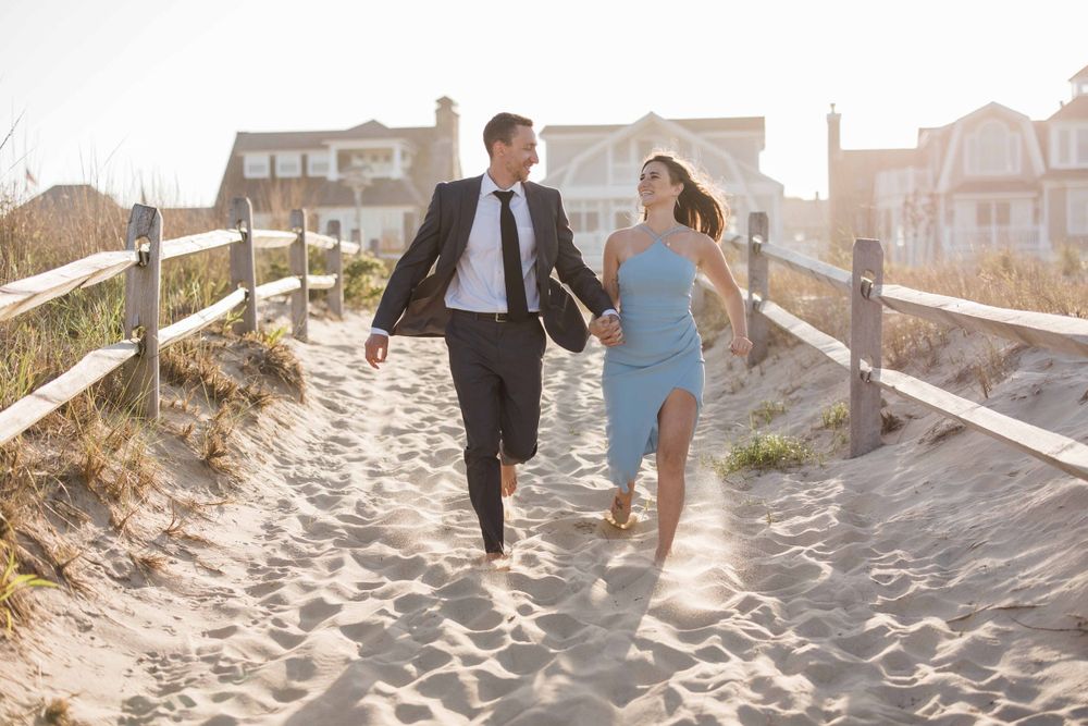 Joyful couple running along sandy beach path between wooden fences at sunset.