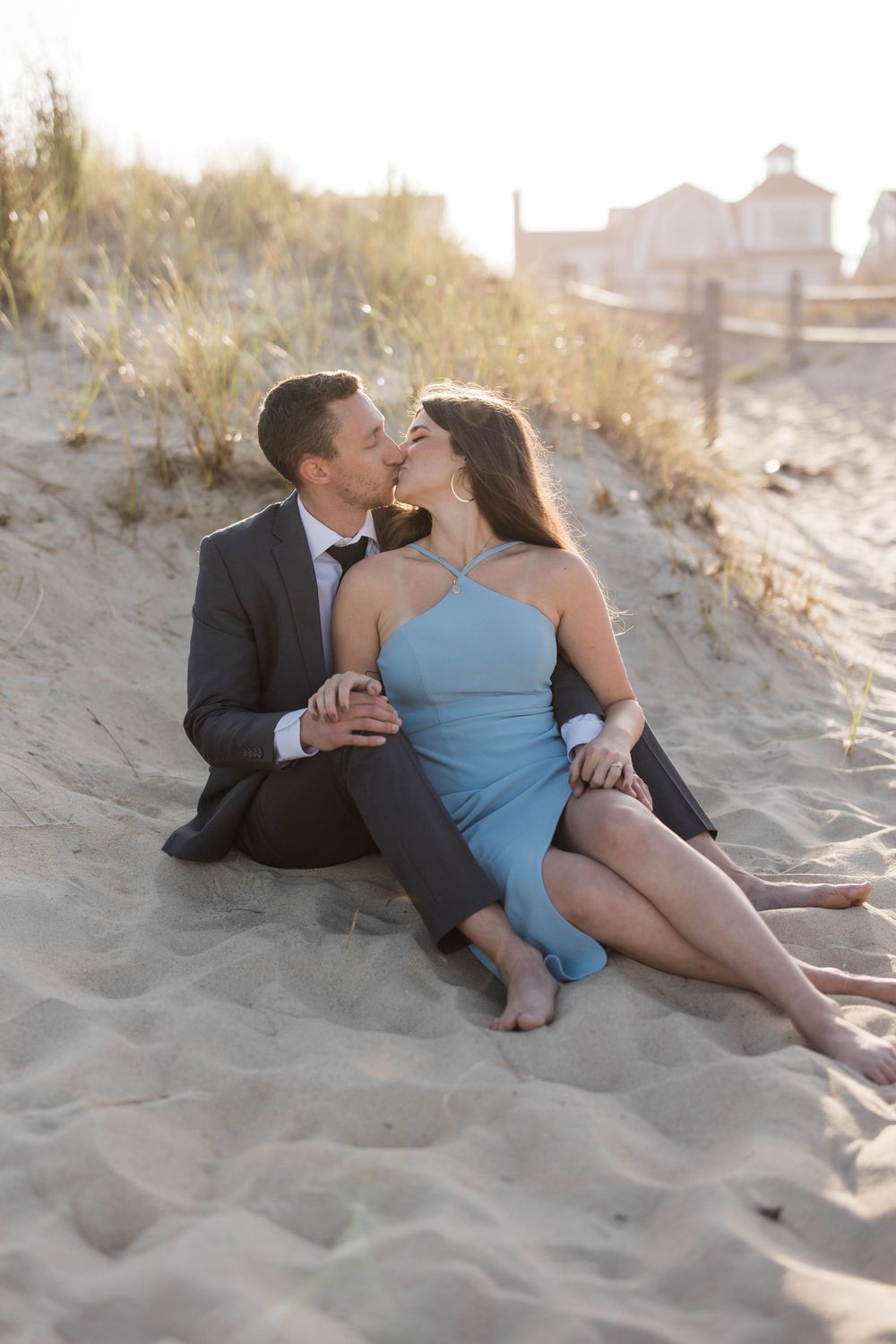 A romantic couple in formal wear embrace on a sandy beach during golden hour.