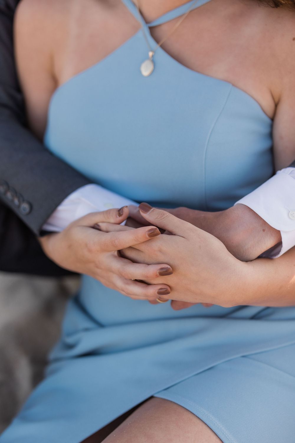 Close-up detail of hands clasped together against a light blue dress.