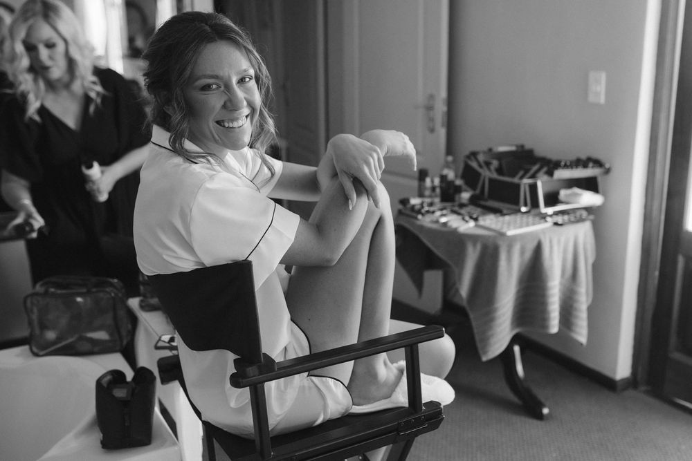 bride smiling while sitting in the make up chair on her wedding day