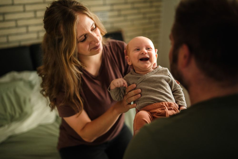 A laughing baby in gray outfit brings smiles during a family moment at home.