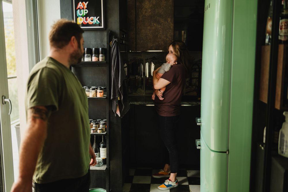 Two people standing in a kitchen space with a mint green refrigerator and shelves of bottles in the background.