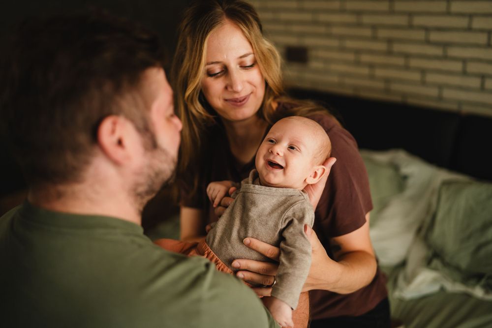 An intimate family scene shows pure joy as a baby smiles between two adults.