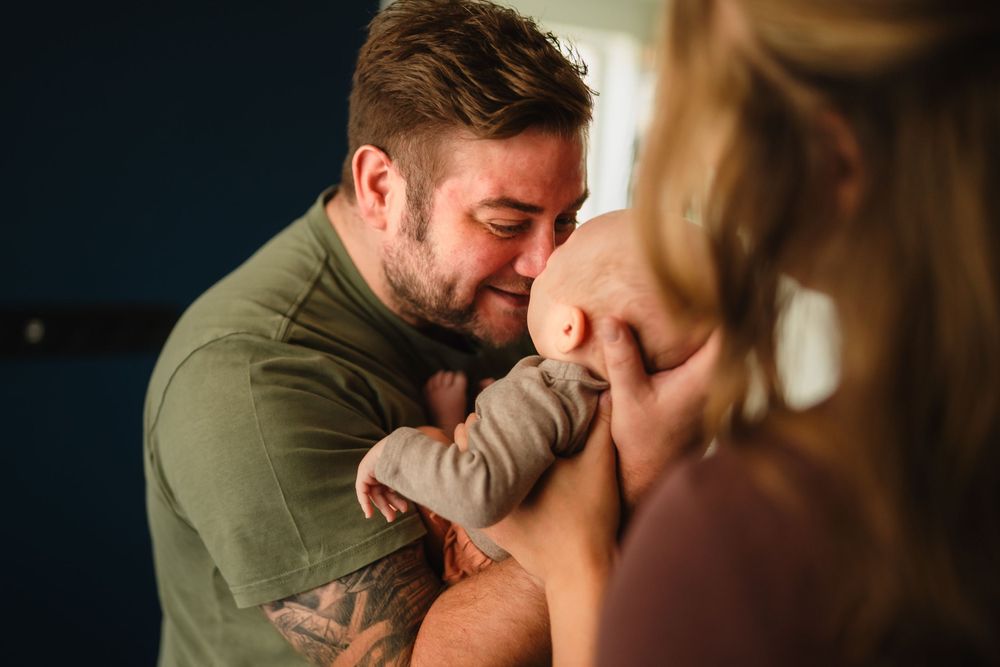 An intimate family moment shows gentle affection with a baby in soft lighting.