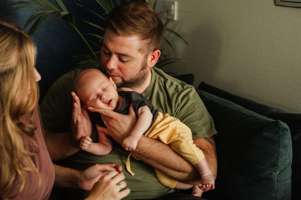 A tender family moment shared on a dark green couch in a sunny living room.