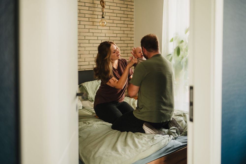 A couple shares an intimate moment while sitting on a bed near a brick wall.