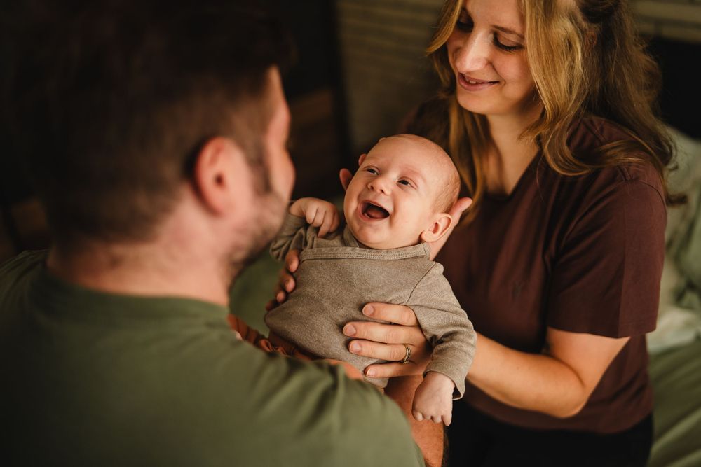 A baby in gray clothing laughs joyfully during a tender family moment.