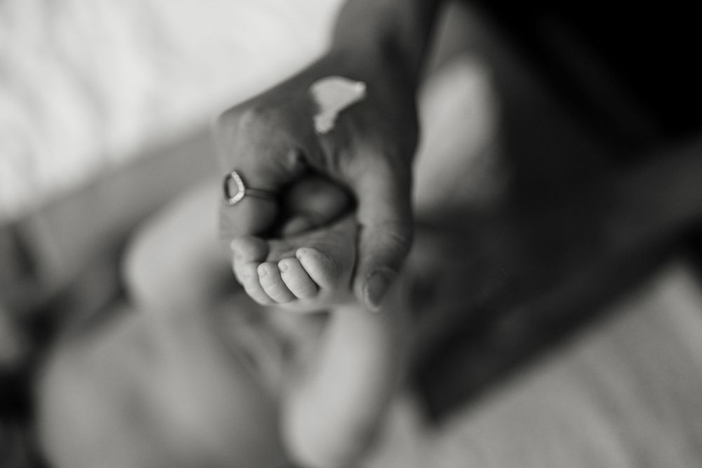 A black and white close-up photograph of a tiny hand being held.