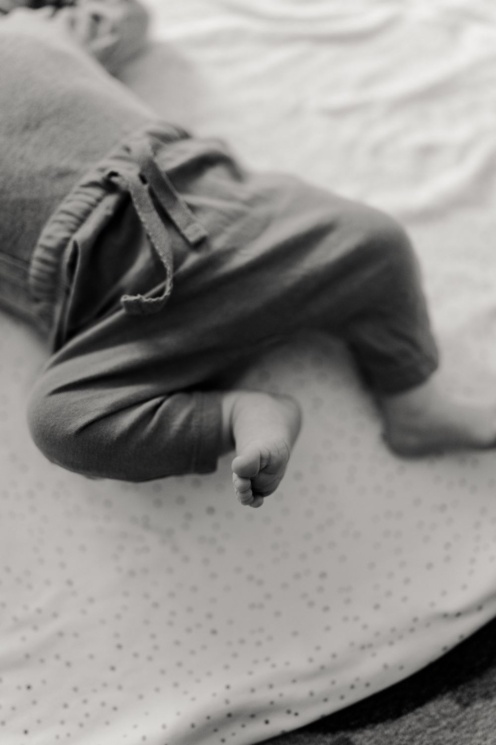 Close-up black and white view of tiny baby feet wearing pants on a polka dot surface.