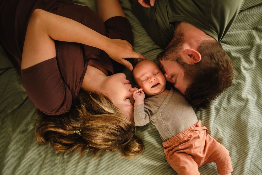 A family lies together on green bedding sharing intimate moments of joy.