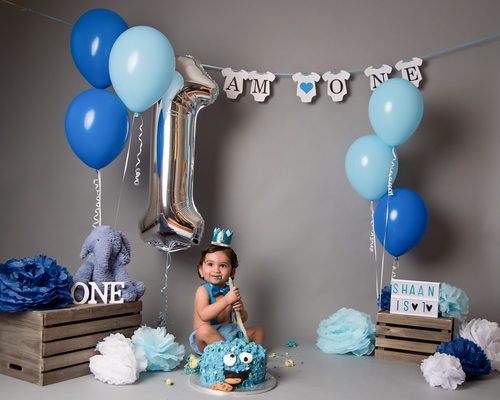 First birthday party setup with blue and white balloons, wooden crates, and party decorations.