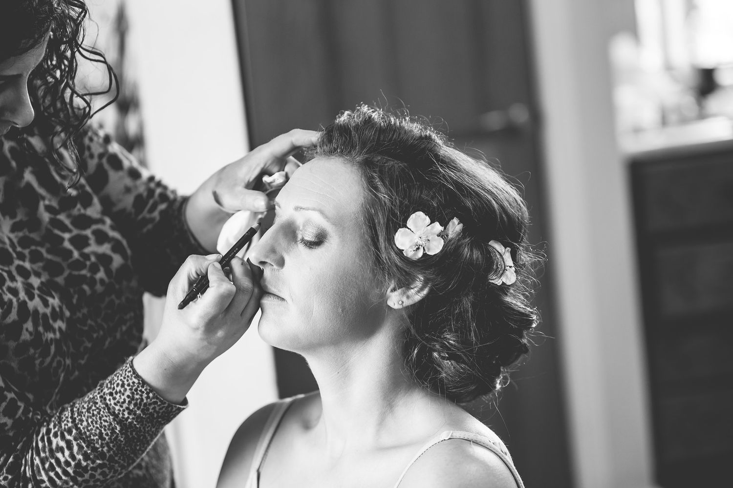 Someone getting makeup applied before a wedding ceremony in black and white.