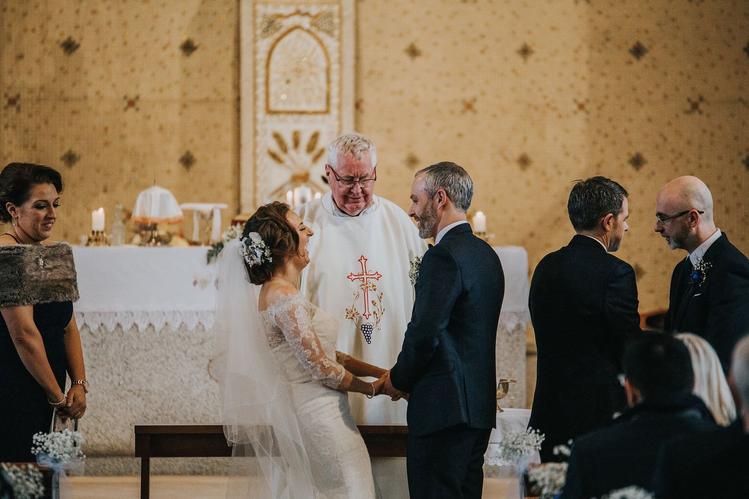 Interior church wedding ceremony with guests seated in pews decorated with candle lanterns.