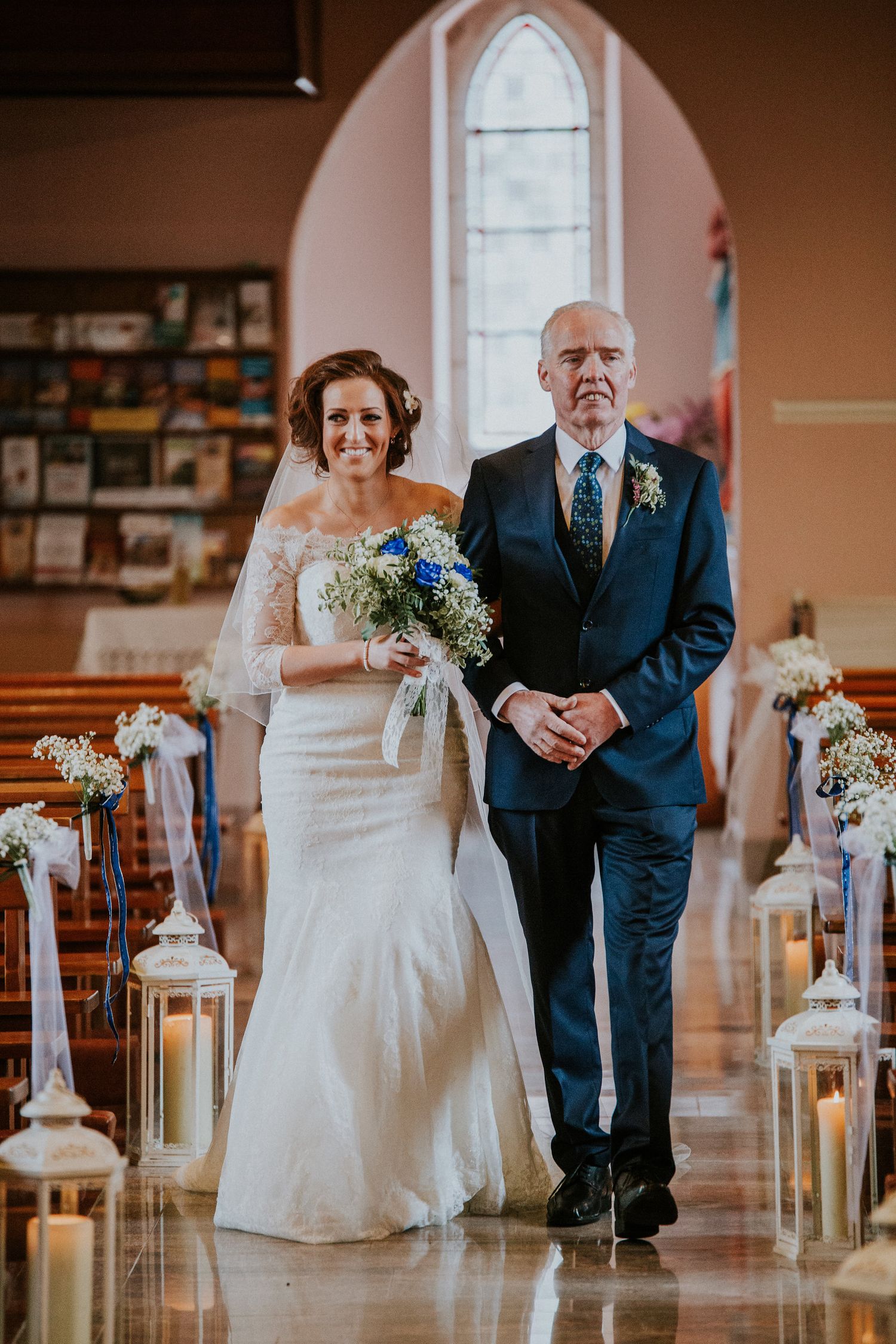 Wedding ceremony processional in church with arched windows and candle decorations.