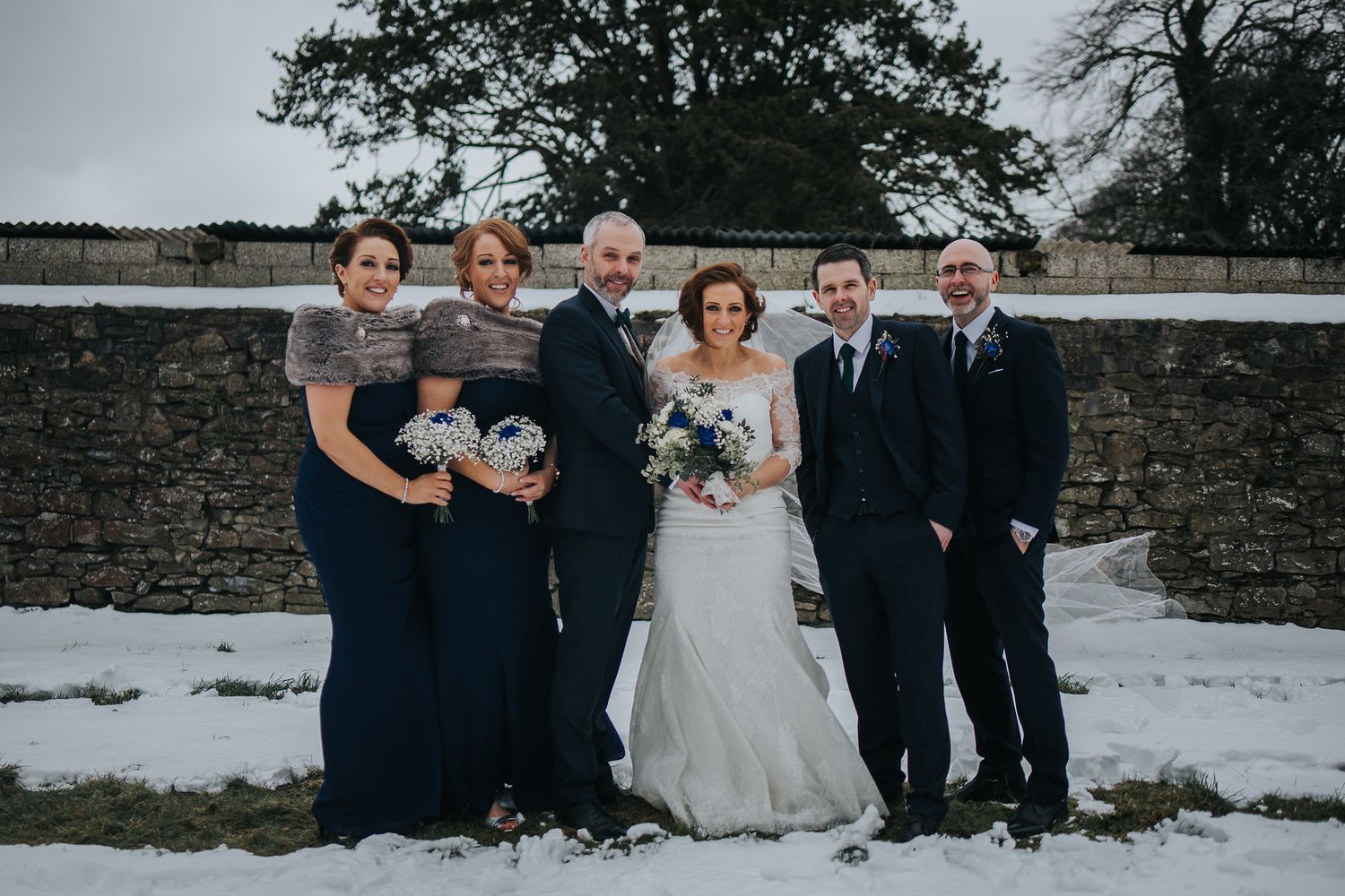 Winter wedding group photo with snow-covered landscape in background.