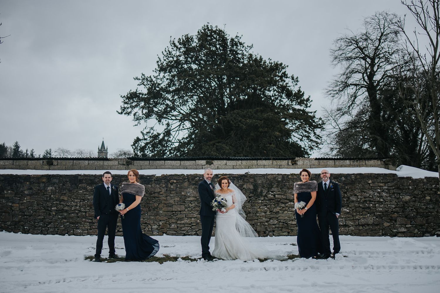 Wedding couple takes romantic photos in snowy winter landscape with trees in background.
