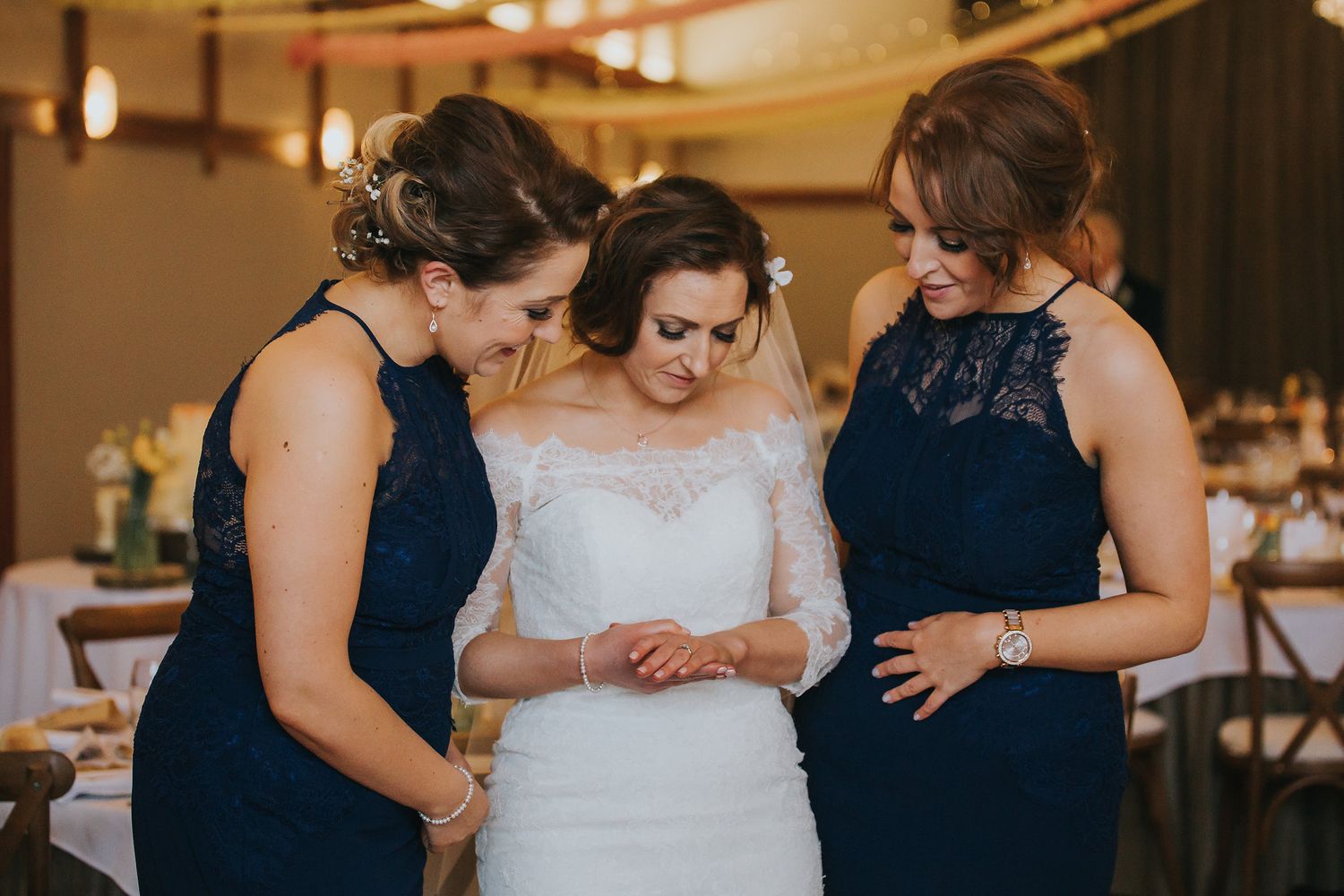 Bridesmaids in navy dresses share emotional moments with bride at indoor wedding venue.