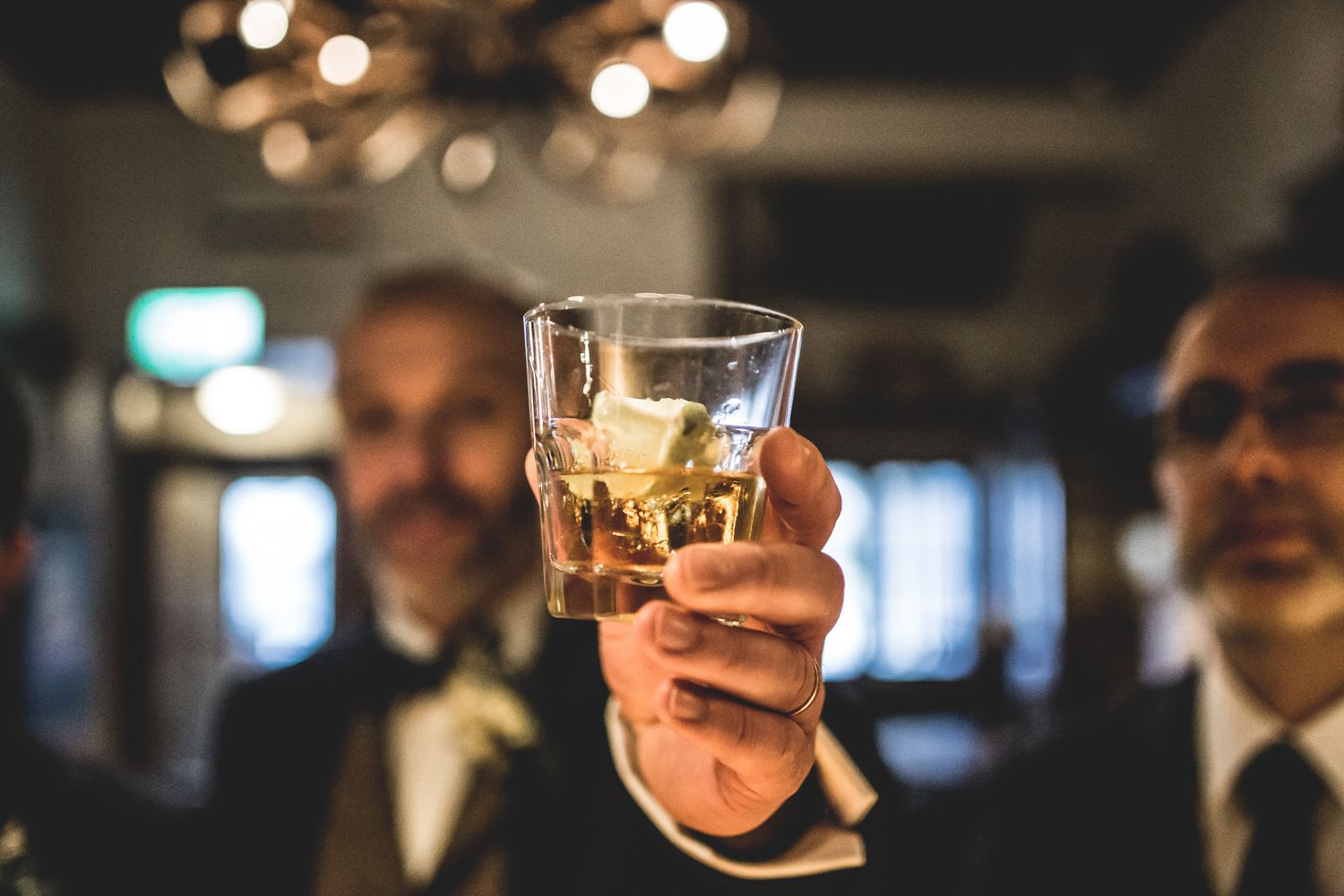 Patrons gather at a dimly lit bar raising glasses in a celebratory toast.