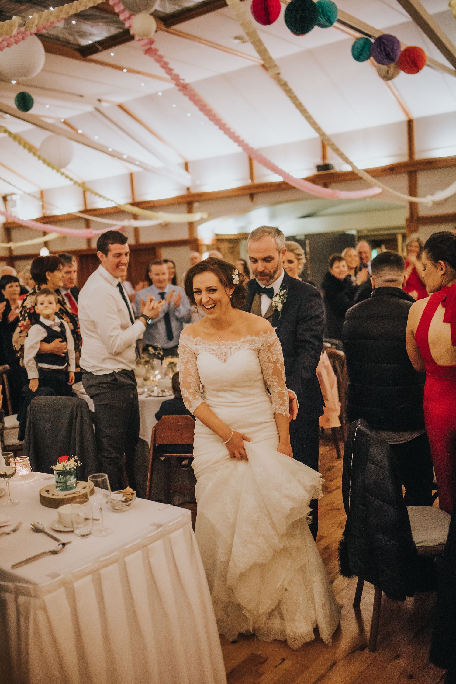 Wedding reception venue decorated with colorful baubles and white linens as guests mingle.