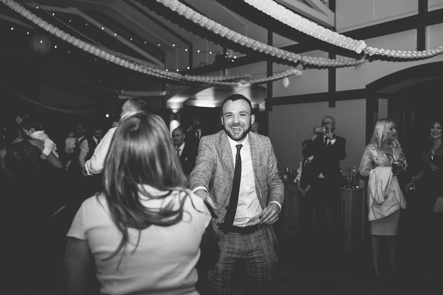 Guests dancing and celebrating at a dimly lit indoor reception venue.