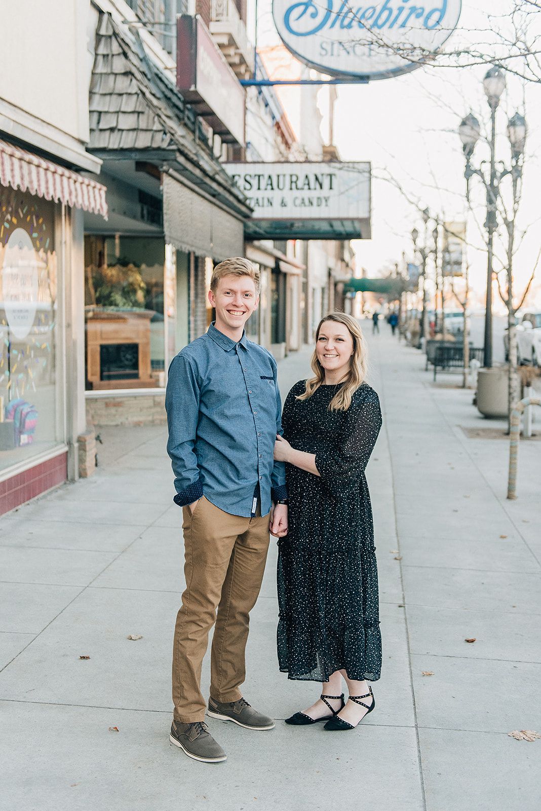 A couple stands outside the Bluebird restaurant on a city sidewalk with classic storefronts and lamp posts.