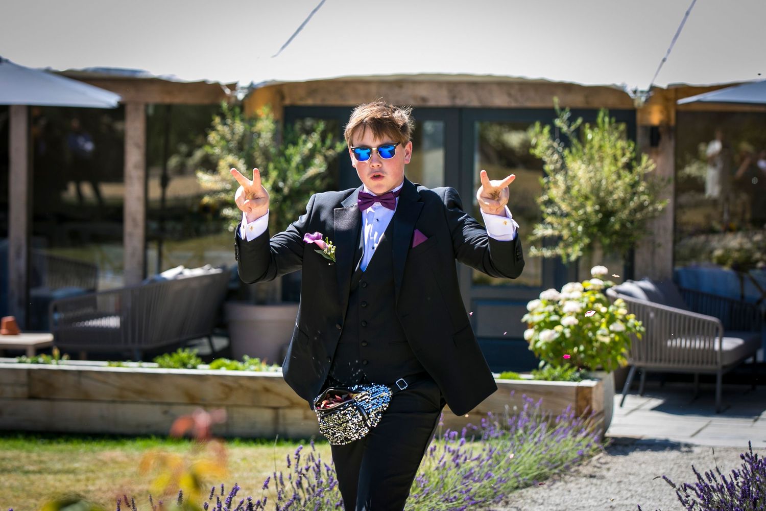 Wedding party members in formal attire striking fun poses in an outdoor garden setting.