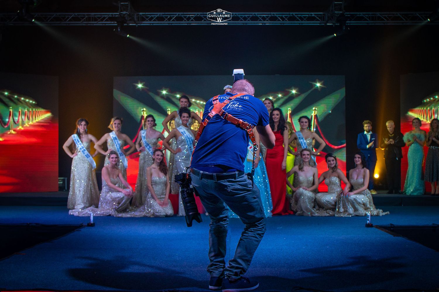 Photographer capturing a group of elegantly dressed women on a stage at a beauty pageant event.