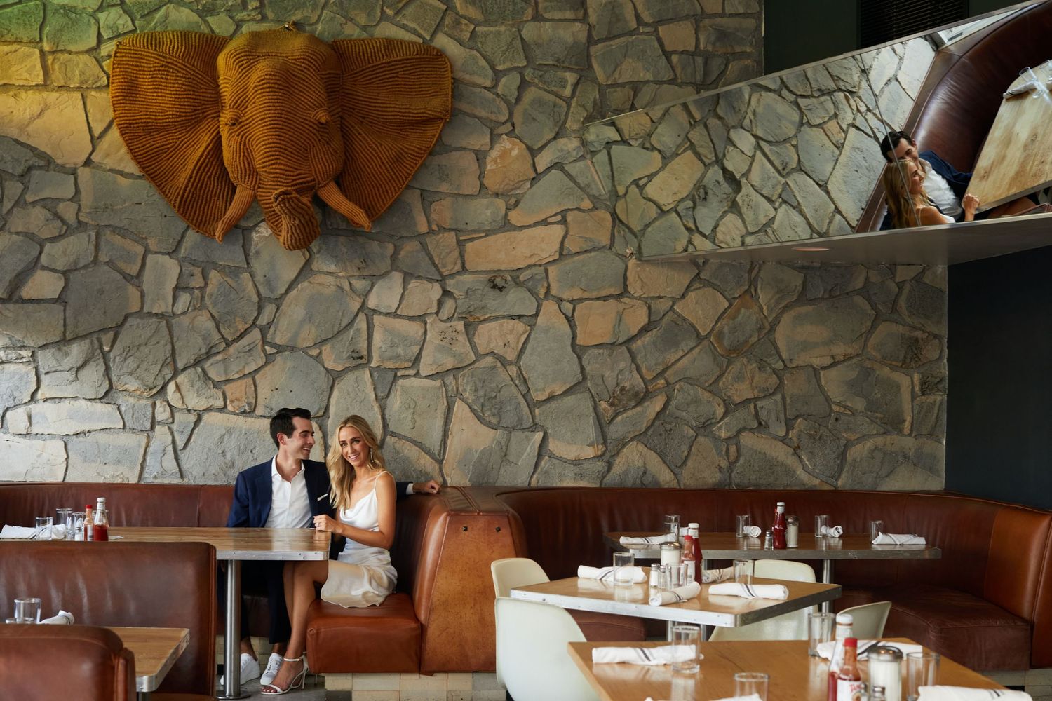 Newlyweds share a moment in a modern restaurant with stone walls and copper elephant decor.