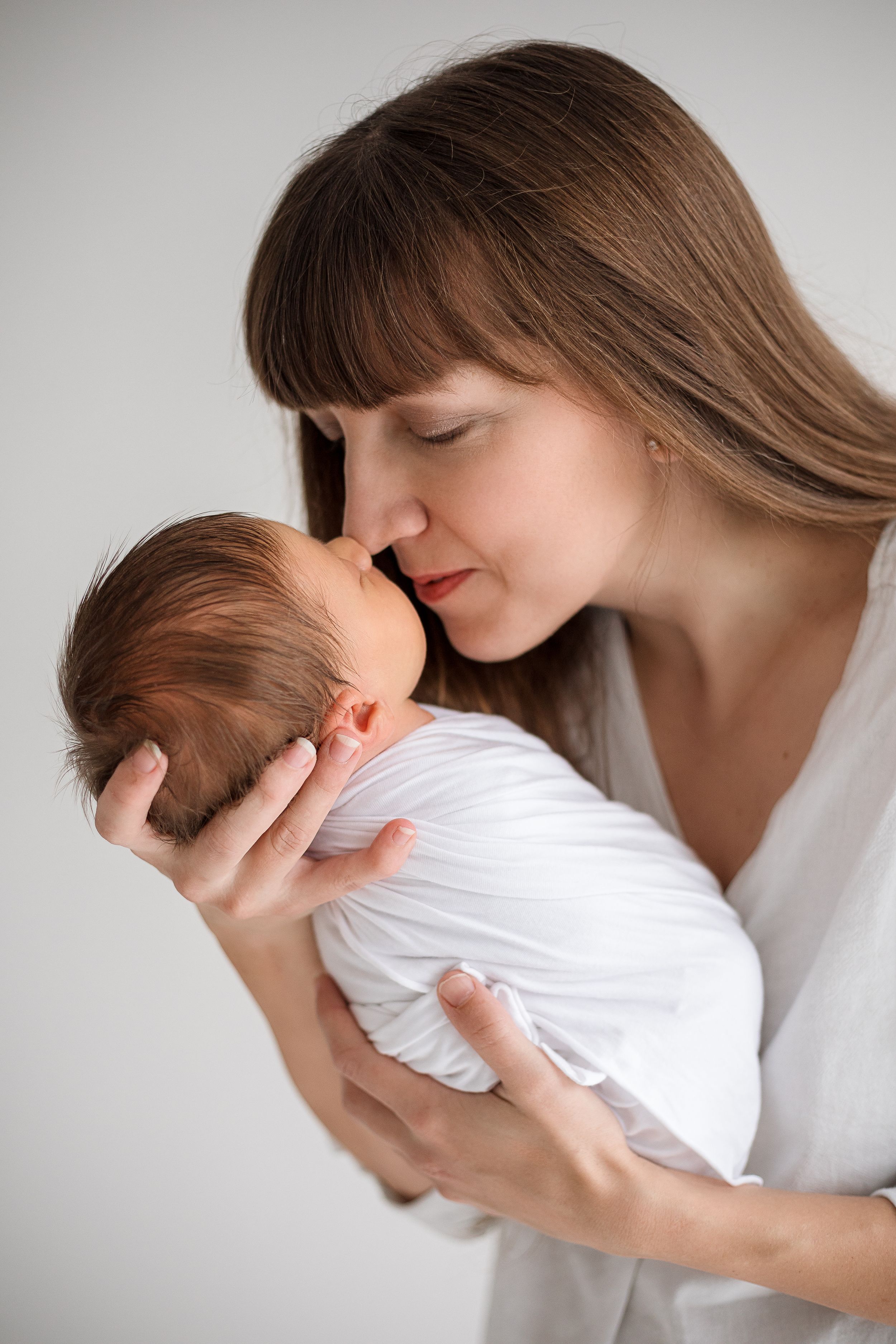 A tender moment between mother and newborn baby in soft lighting against a neutral background.
