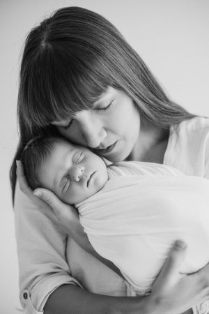 Black and white intimate portrait of mother and sleeping newborn baby.