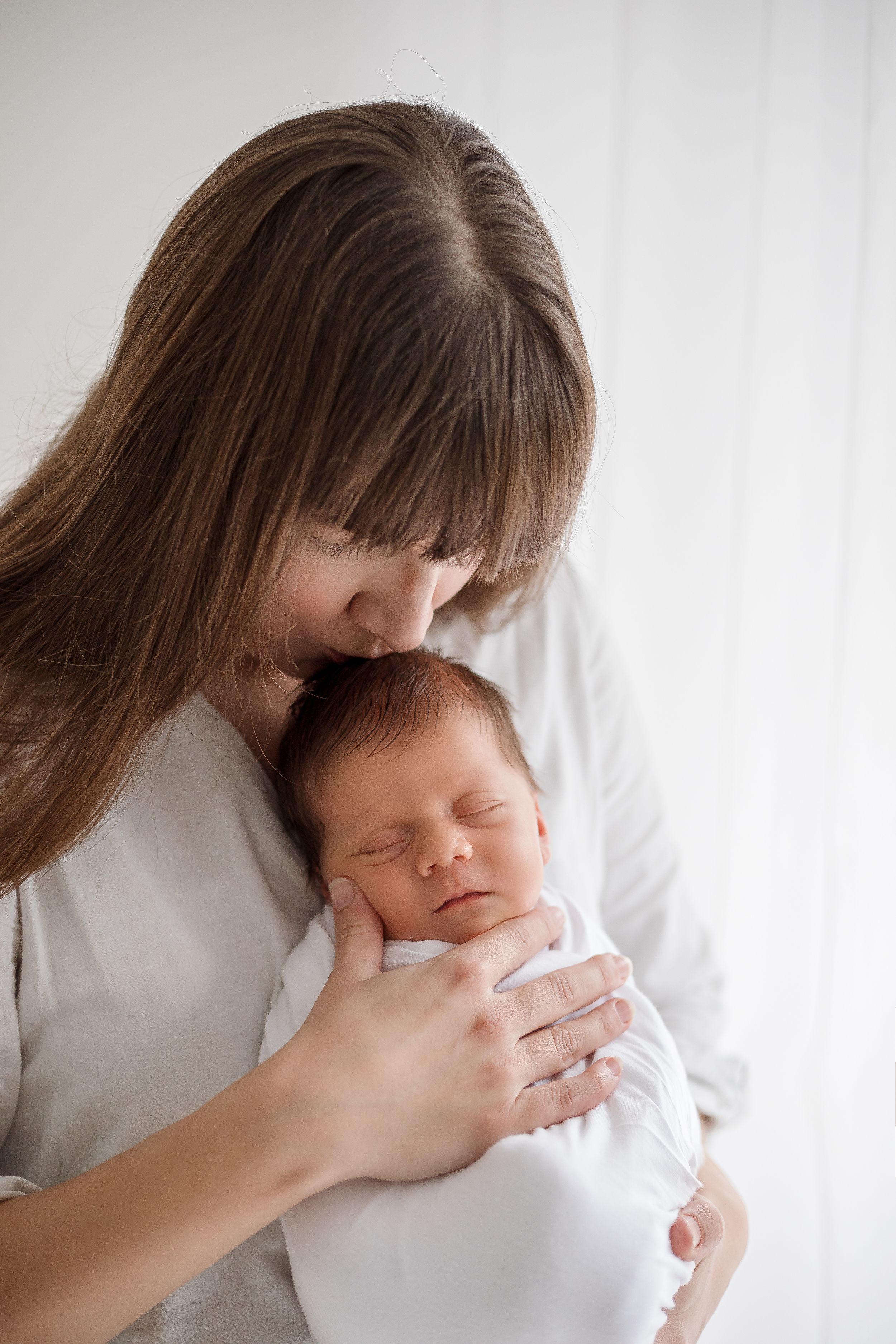 Intimate newborn portrait showing tender moment against soft white background.