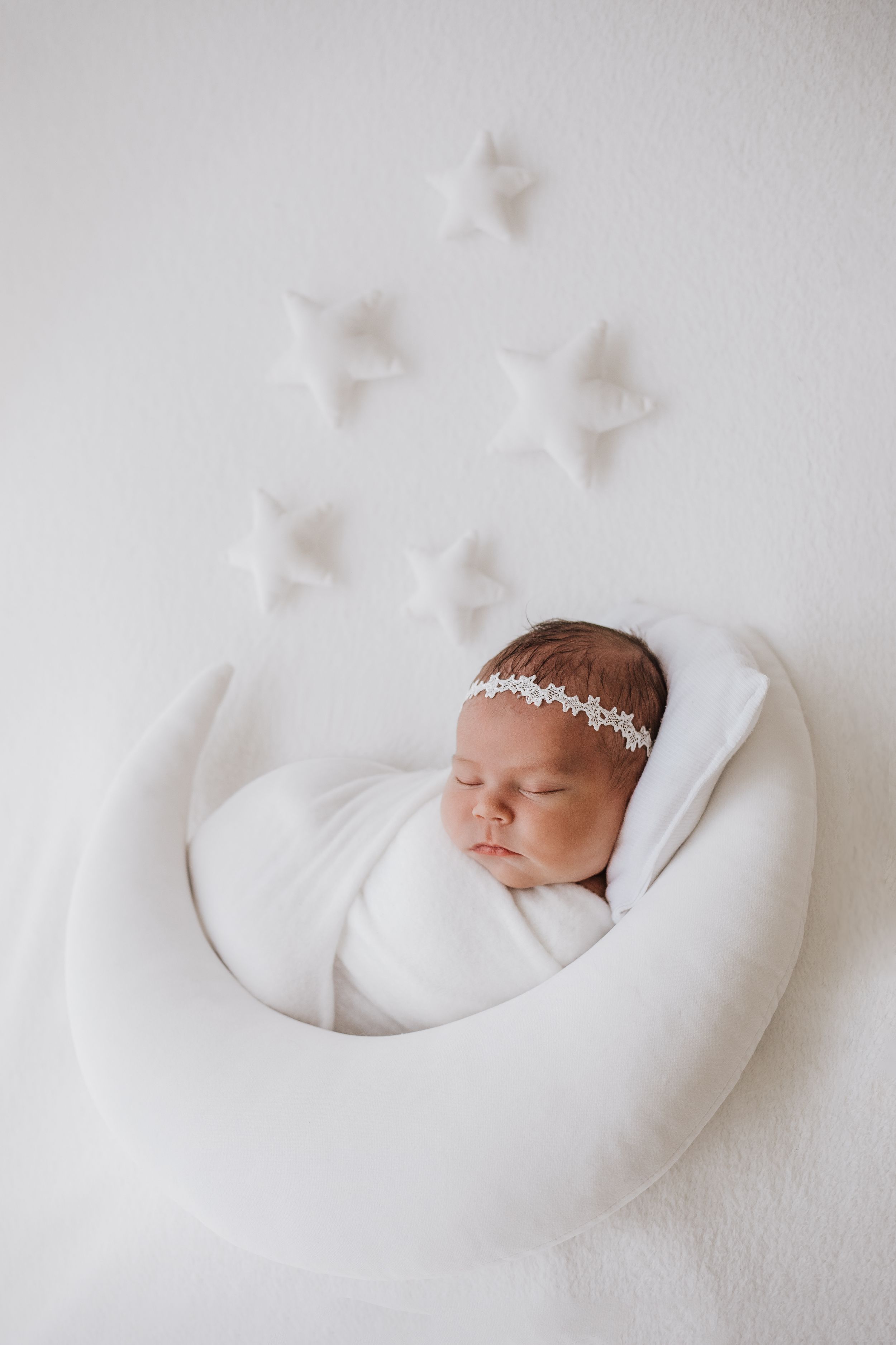 Newborn baby sleeping peacefully on white cushion with decorative stars above.