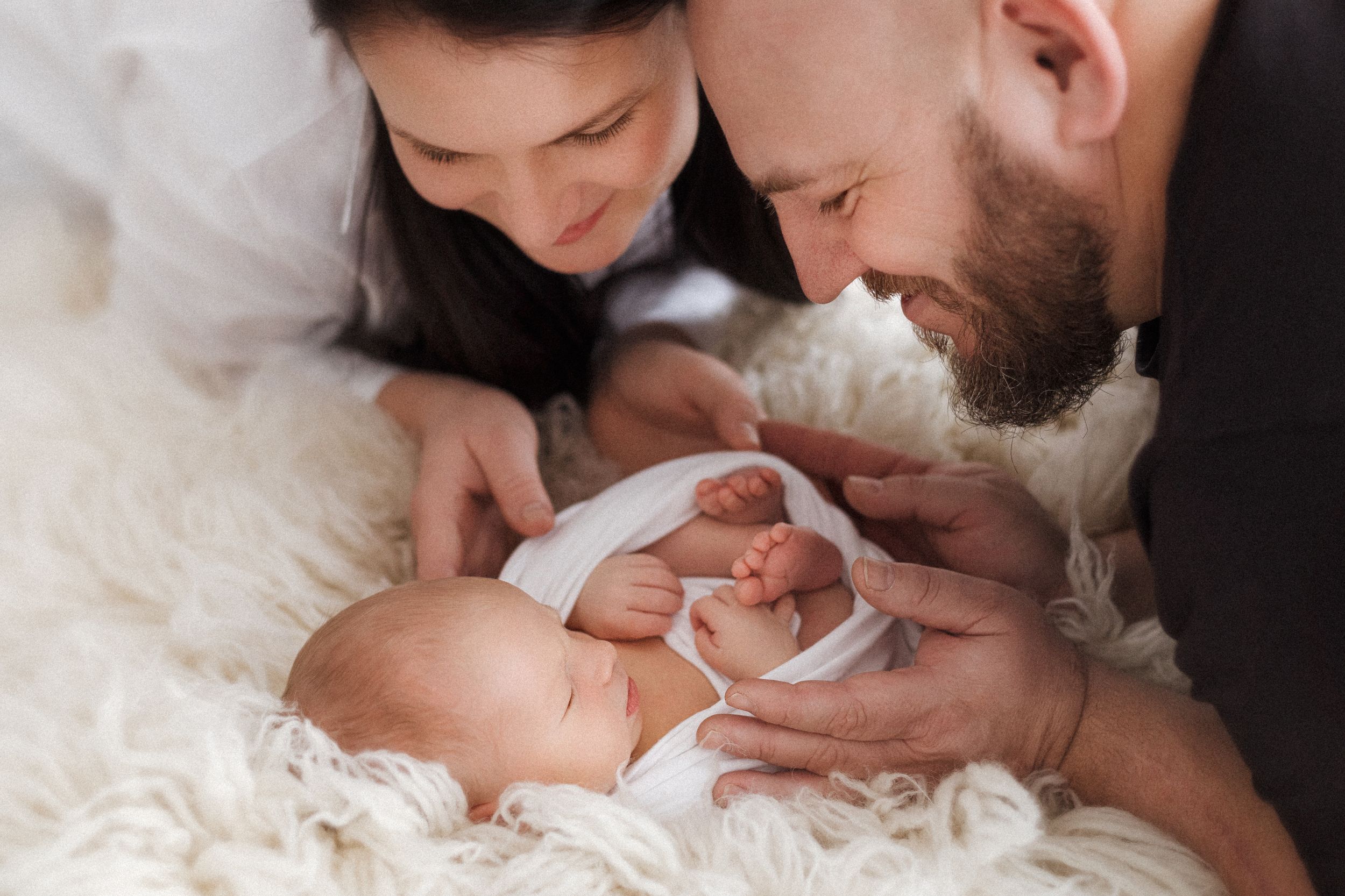 Intimate family moment with new parents admiring their newborn baby on soft white bedding.