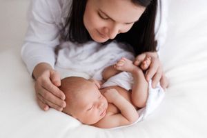 Gentle moment between parent and sleeping newborn baby on white bedding.