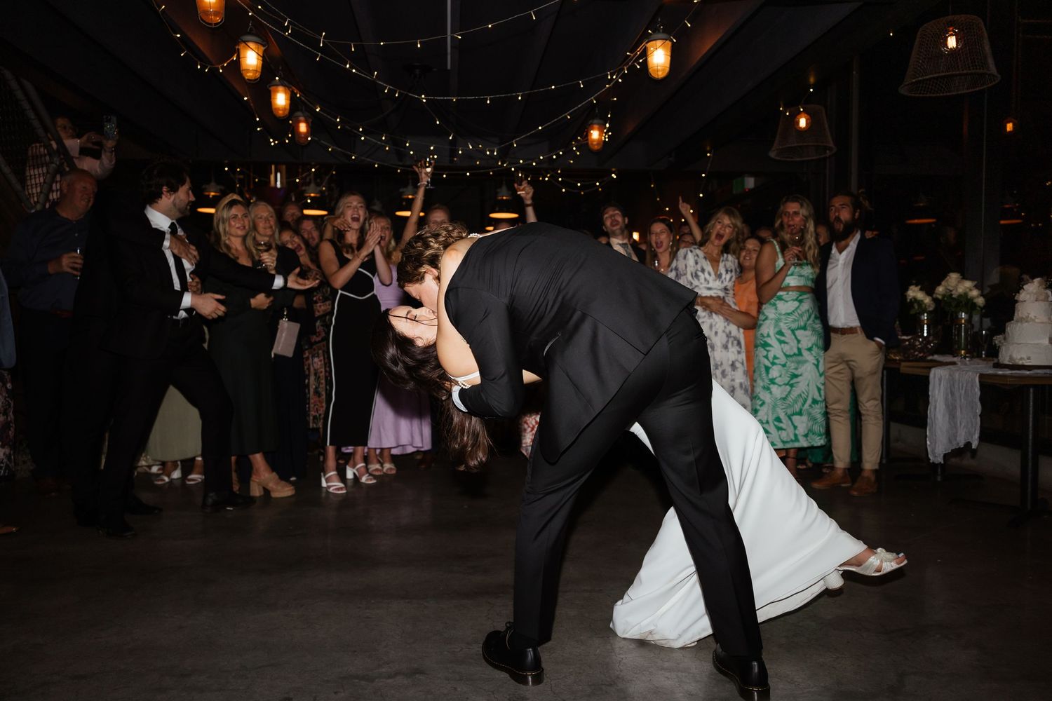 Romantic dip during first dance at wedding reception with string lights overhead.