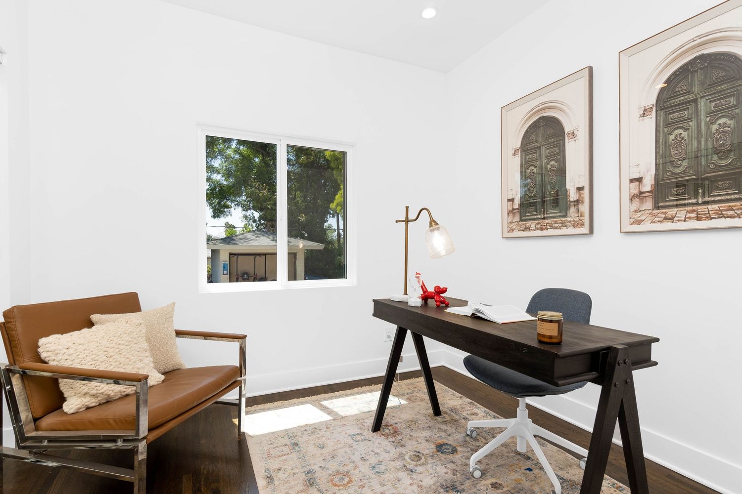Stylish home office with leather accent chair, dark wood desk and framed architectural prints.