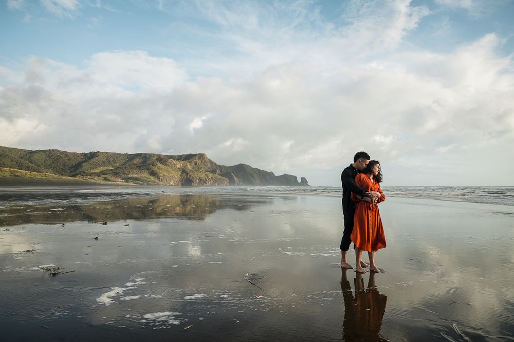 August and Vine wedding photography of couple embracing reflected in the sand at bethells beach
