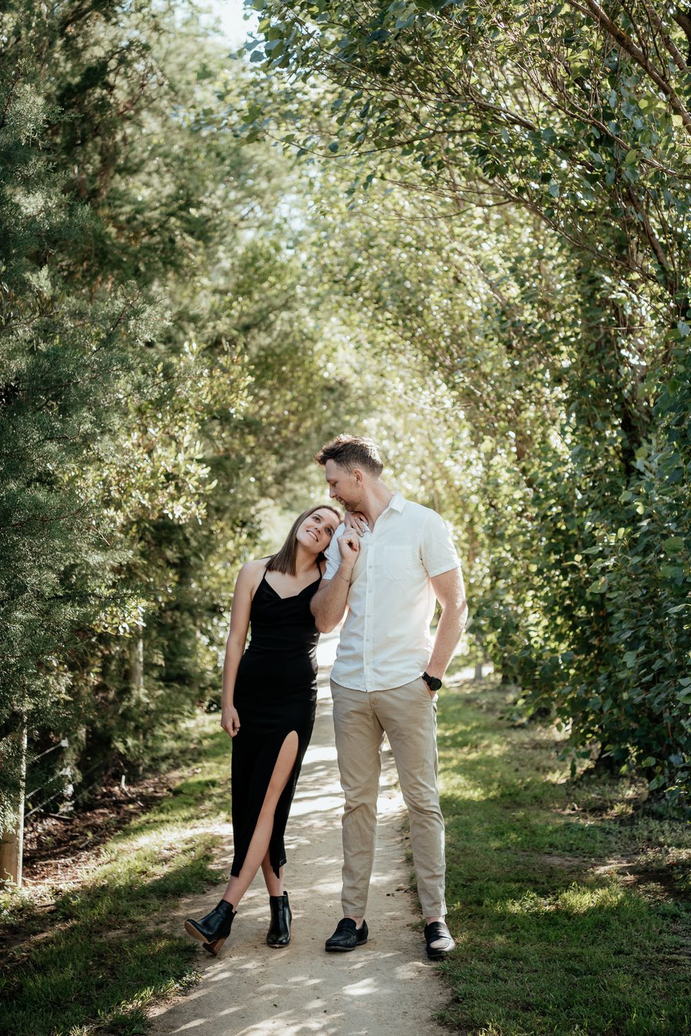 Couple stand in an arch of shrubs looking at each other lovingly by August and Vine