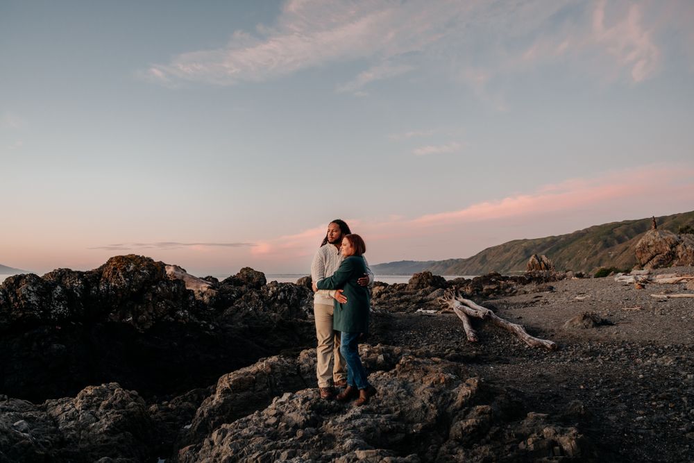 Couple stand on the rocks at sunset at Pukerua Bay Wellington by August and Vine