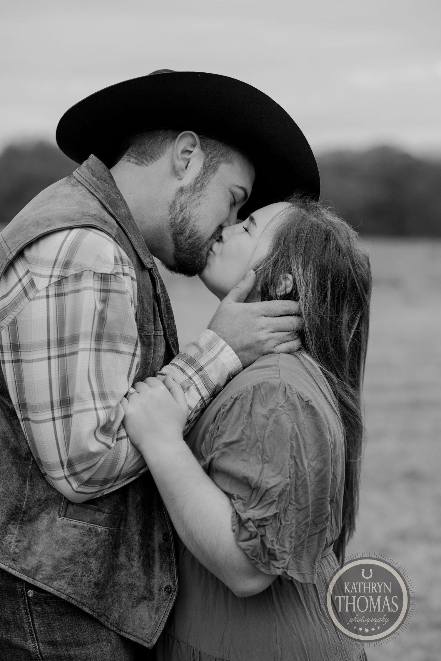 An intimate black and white photo captures a tender moment between a couple in western attire.