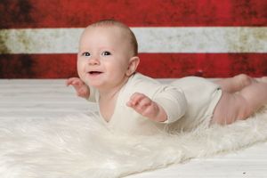 Baby in white outfit on fur blanket with red and white striped background.