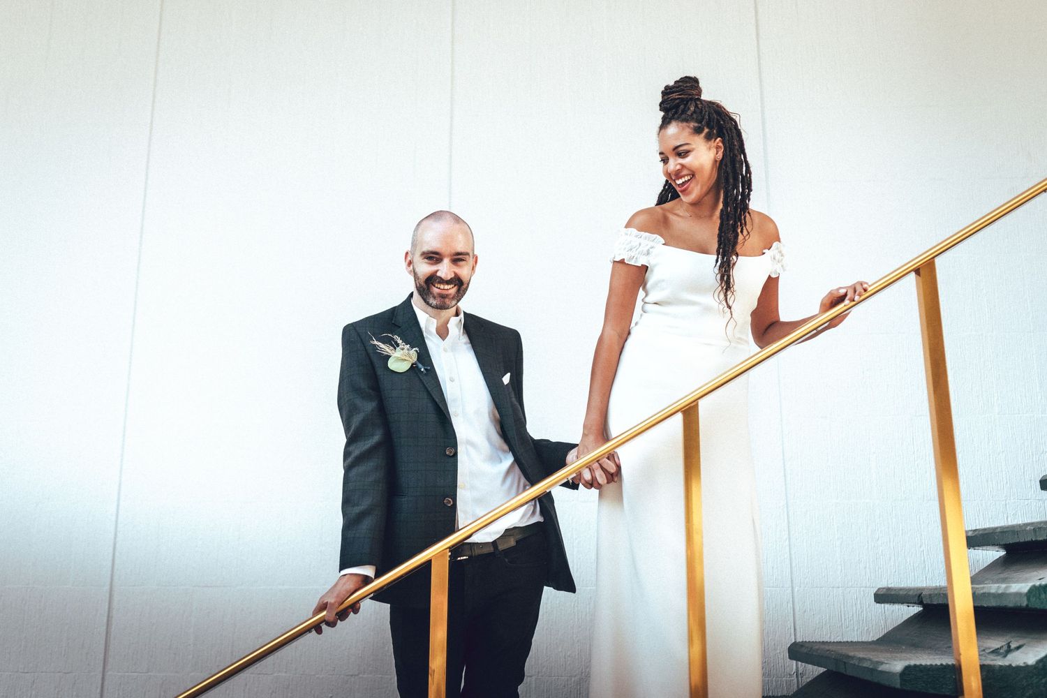 Elegant wedding couple standing on staircase with gold railing in contrasting black and white attire.