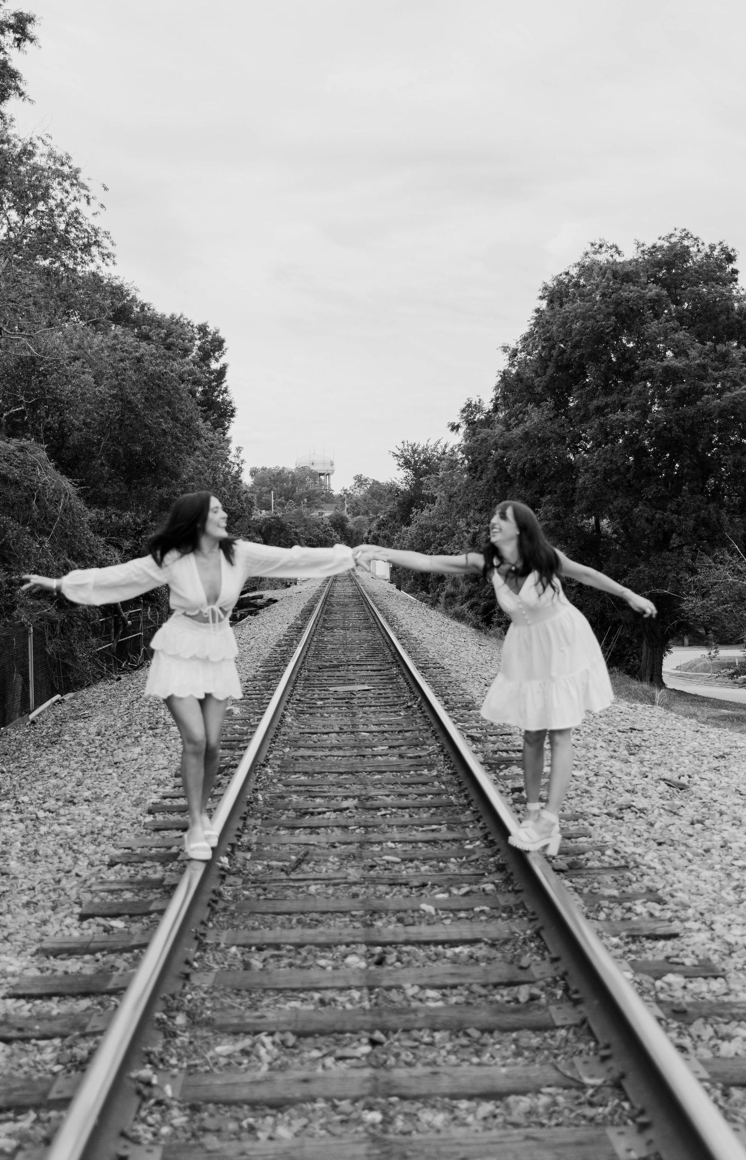 Black and white grad photo of two girls walking on railroad tracks in white dresses.