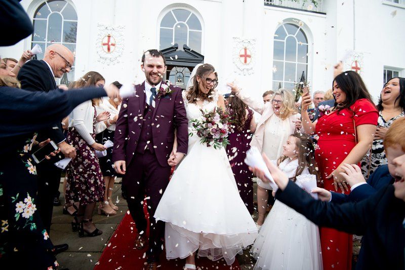 Newlyweds exit church while guests shower them with white confetti on their wedding day.