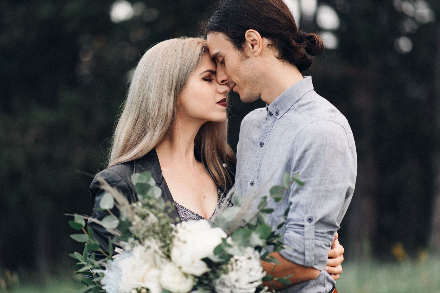 Intimate moment between couple holding white floral bouquet outdoors.