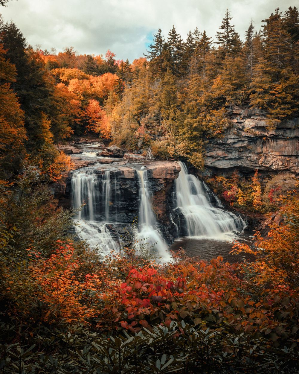 Stunning waterfall cascades down rocky cliffs surrounded by vibrant autumn foliage in a forest landscape.