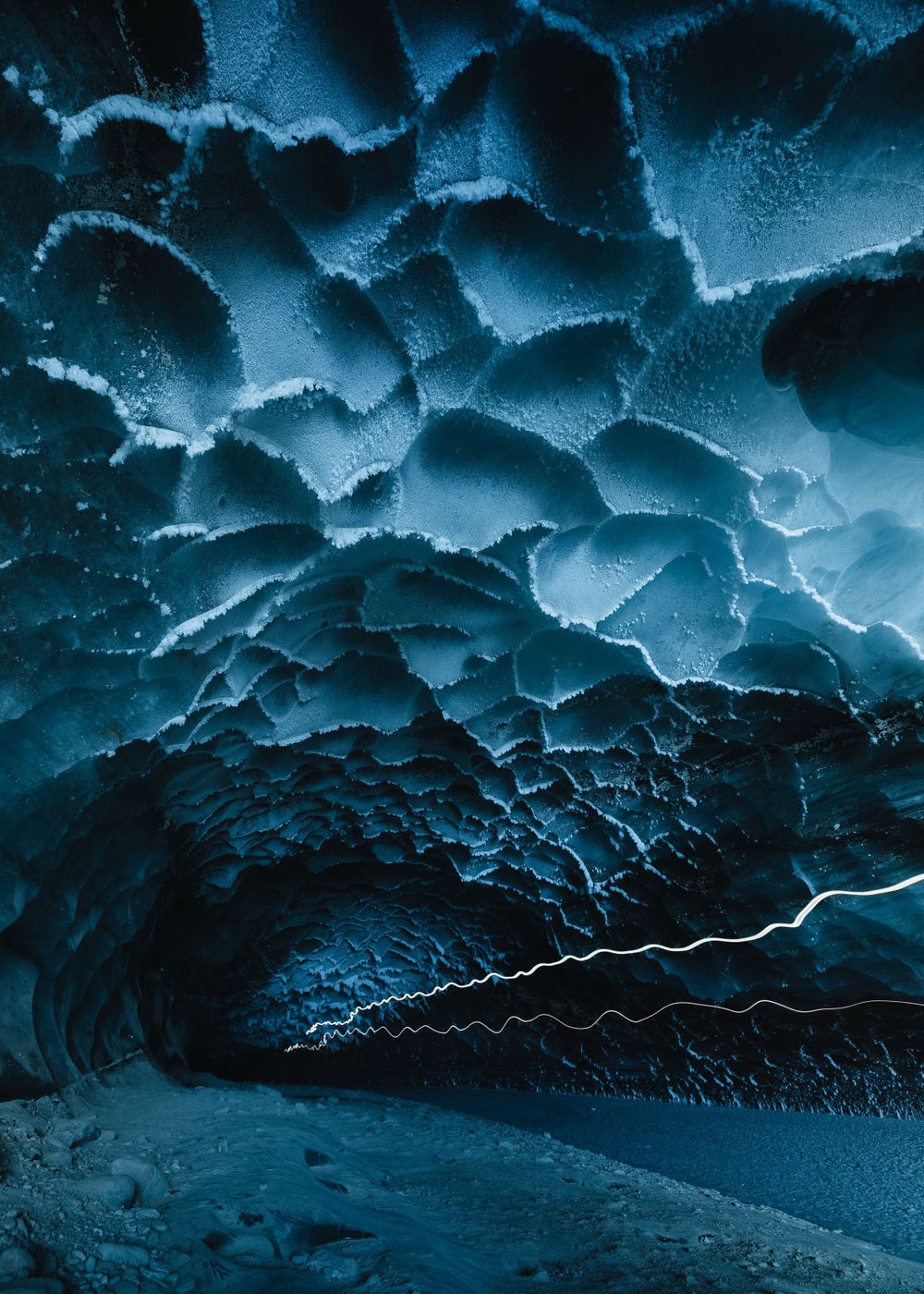 Ice cave with intricate blue patterns forming on its crystalline ceiling.