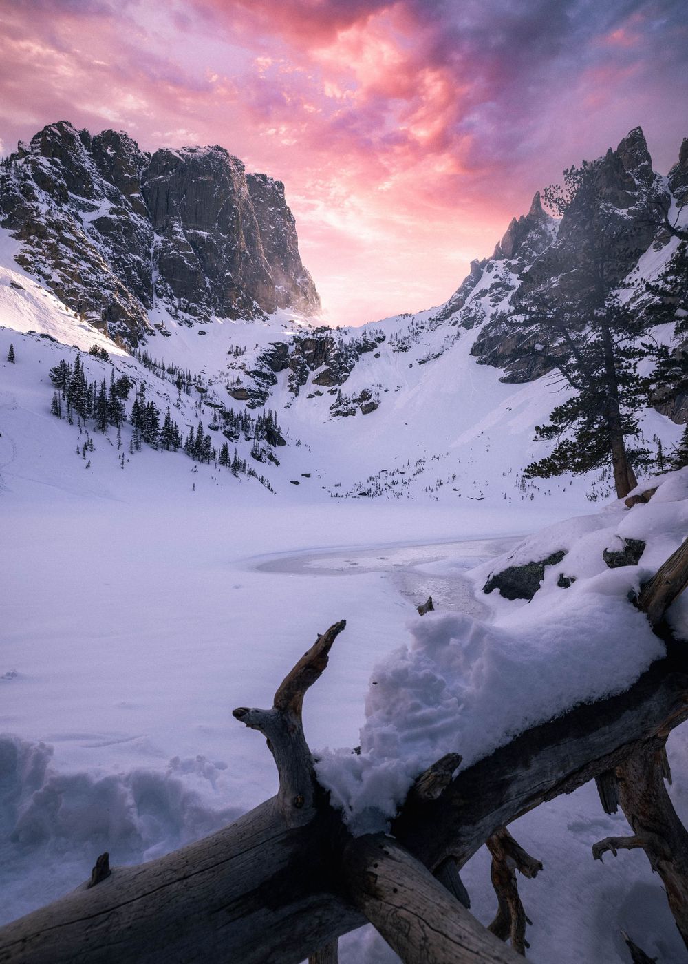 Dramatic sunset illuminates snow-covered mountain peaks with vibrant pink and purple skies.