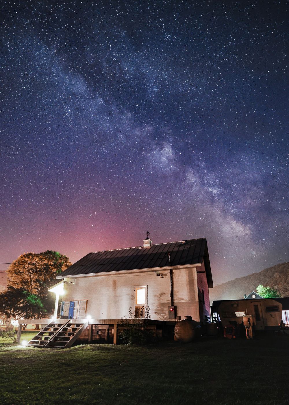 Small illuminated house under a spectacular Milky Way night sky.